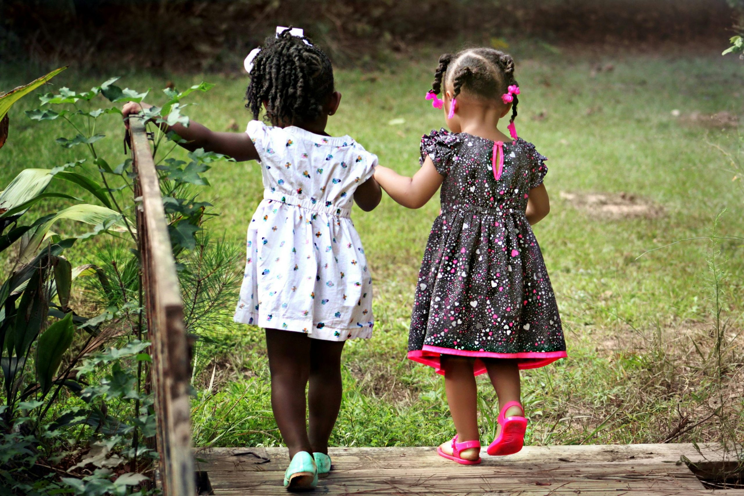 Two young girls in colorful dresses walking hand in hand outdoors, embodying friendship and innocence.