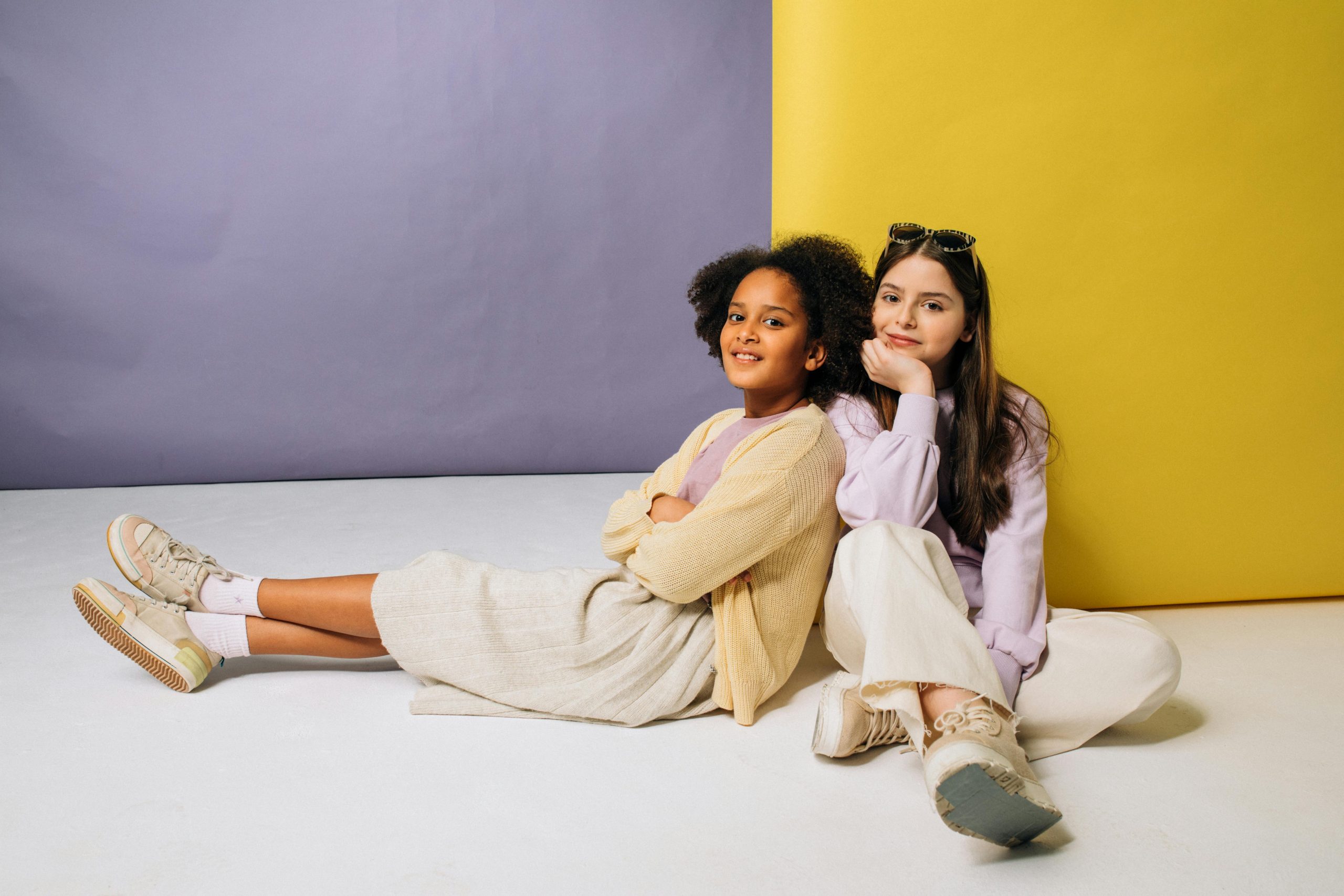 Two smiling girls relaxing against a vibrant backdrop, showcasing friendship.