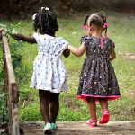 Two young girls in colorful dresses walking hand in hand outdoors, embodying friendship and innocence.