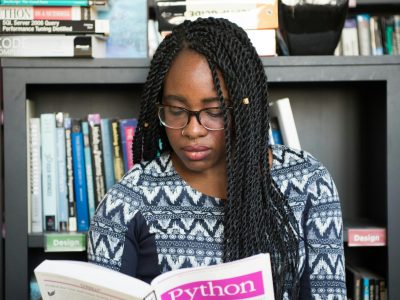 African American woman studying Python programming in a library setting.