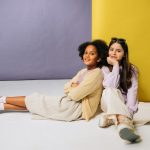 Two smiling girls relaxing against a vibrant backdrop, showcasing friendship.