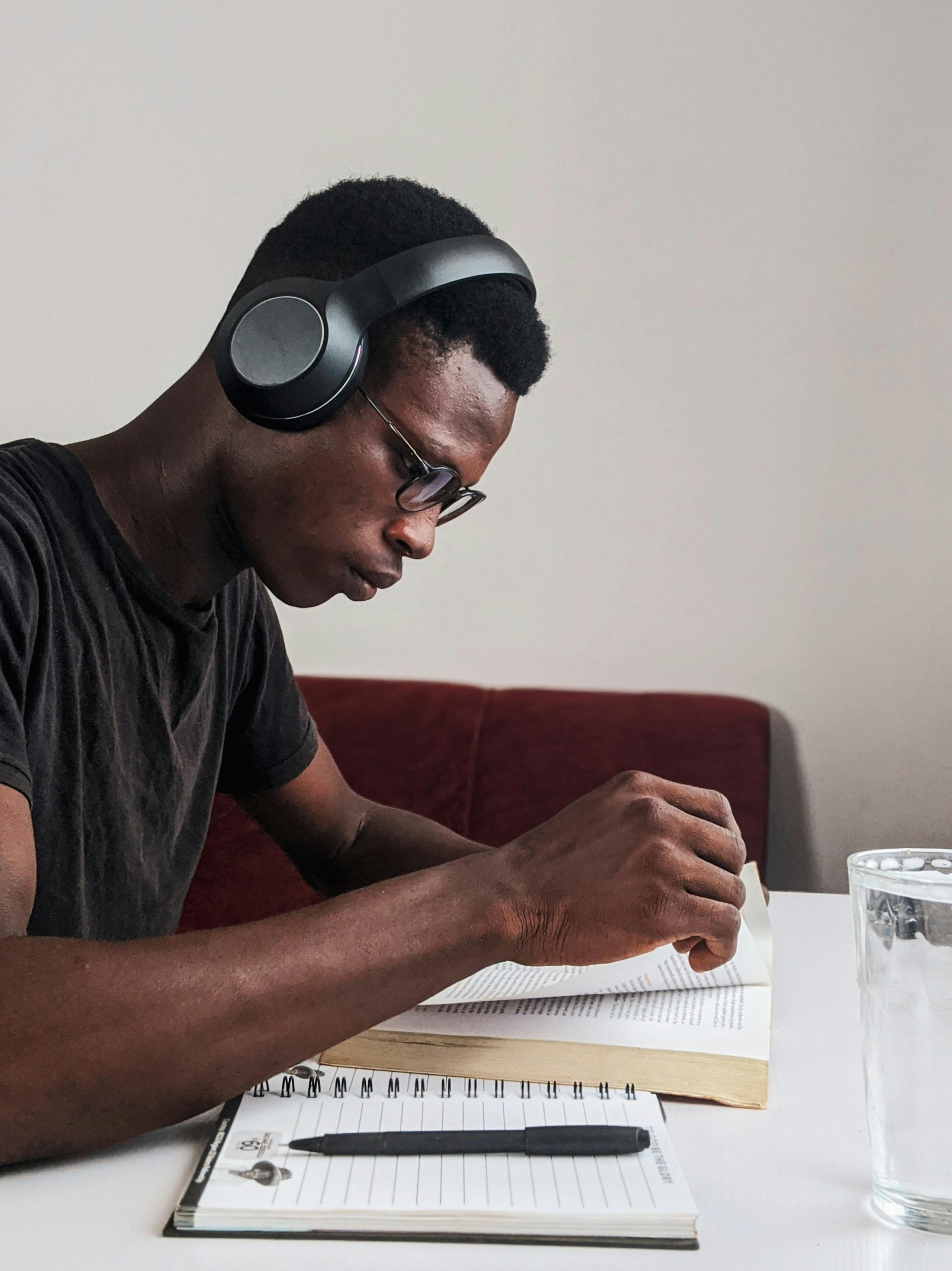 pexels-photo-3466163-3466163 An adult man intensely studying with headphones, pen, and notebook at a desk indoors.